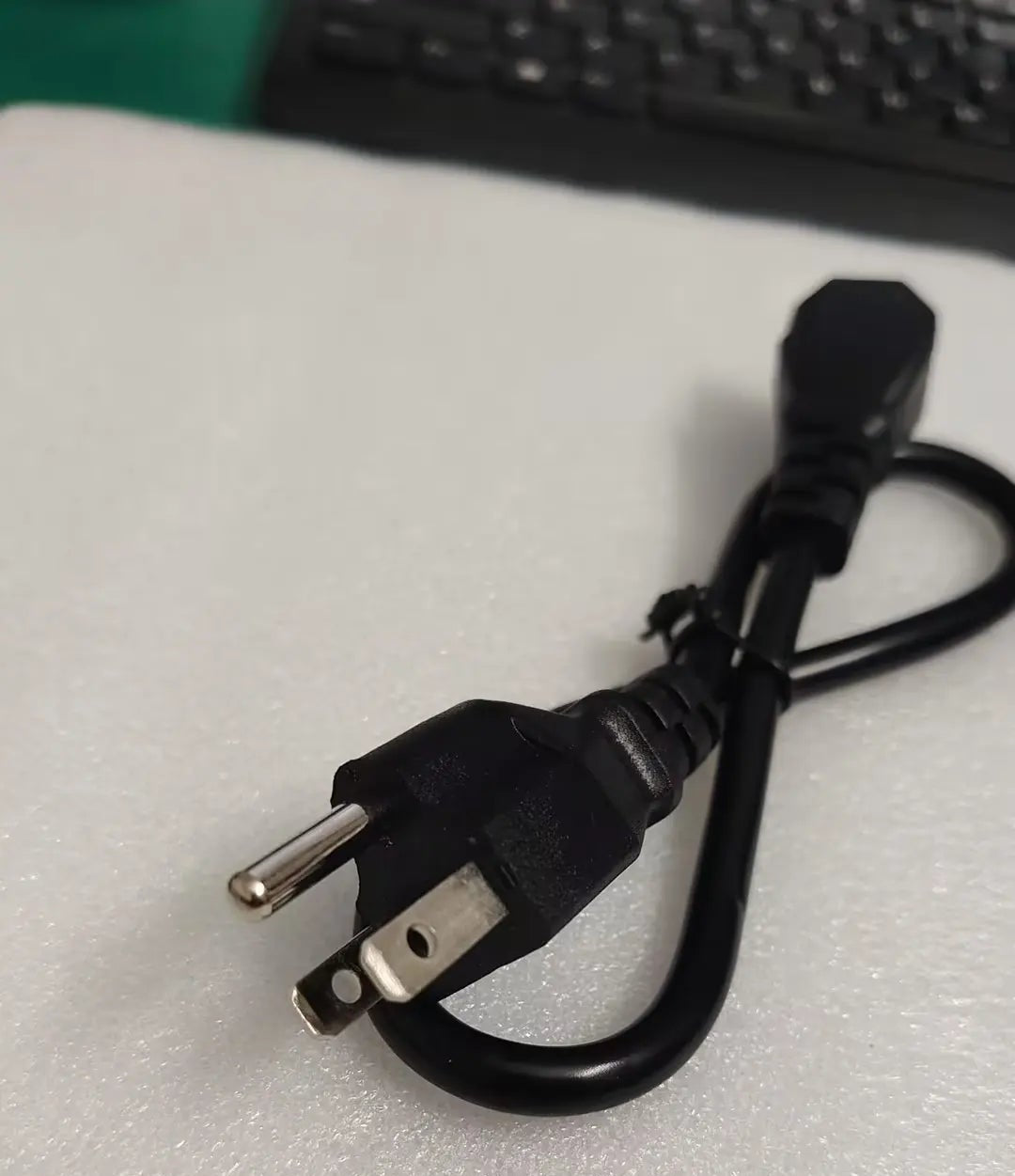 A black power cord with a two-prong US plug, resting on a textured white surface.
